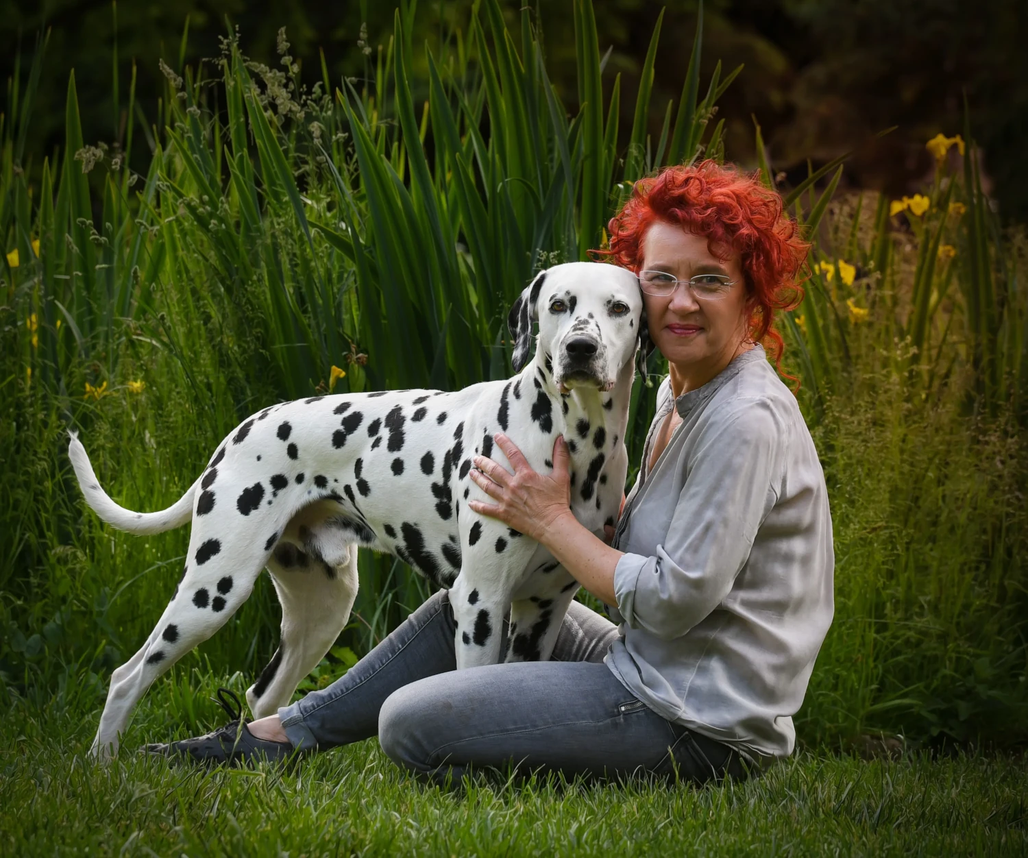 Frau mit roten Locken kniet im Garten und umarmt einen Dalmatiner Hund.